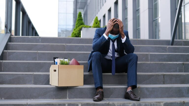 Man sitting on stairs with head in his hands and a box filled with office supplies next to him. Meant to illustrate constructive dismissal Canada