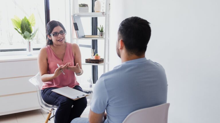 Woman occupational therapist with male patient telling about mental problems while doctor is listening and making notes.